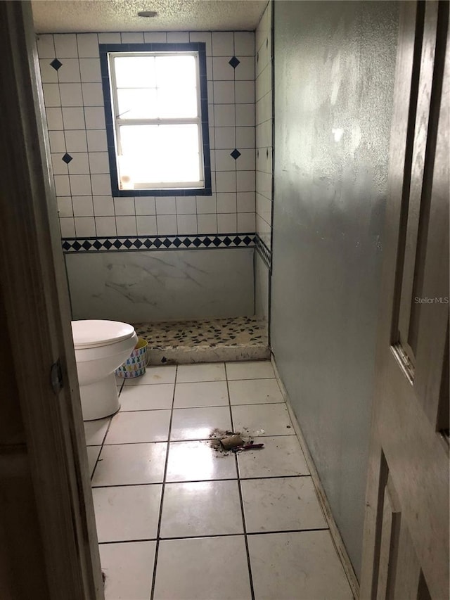 bathroom with tile patterned flooring, a tile shower, a textured ceiling, and toilet