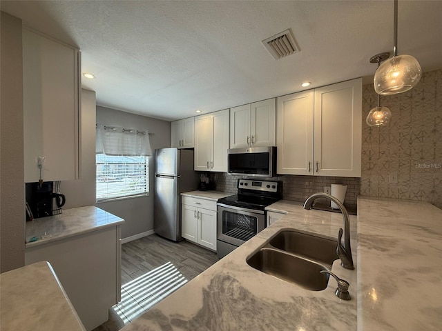 kitchen featuring white cabinetry, sink, light stone countertops, hanging light fixtures, and stainless steel appliances