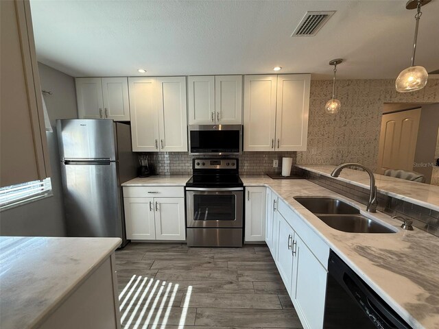 kitchen featuring pendant lighting, backsplash, white cabinets, sink, and stainless steel appliances