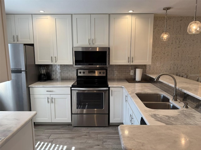 kitchen with white cabinets, hanging light fixtures, sink, decorative backsplash, and appliances with stainless steel finishes