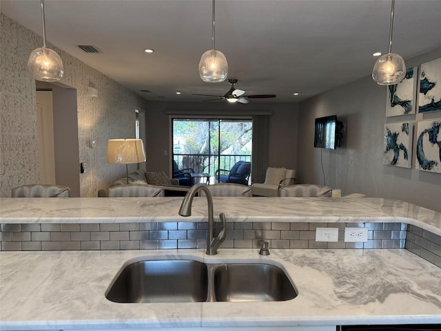 kitchen with light stone counters, sink, ceiling fan, and decorative light fixtures