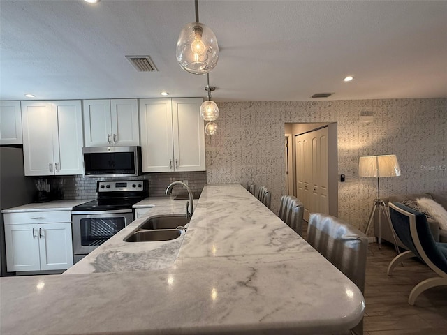 kitchen with decorative light fixtures, light stone counters, white cabinetry, and appliances with stainless steel finishes