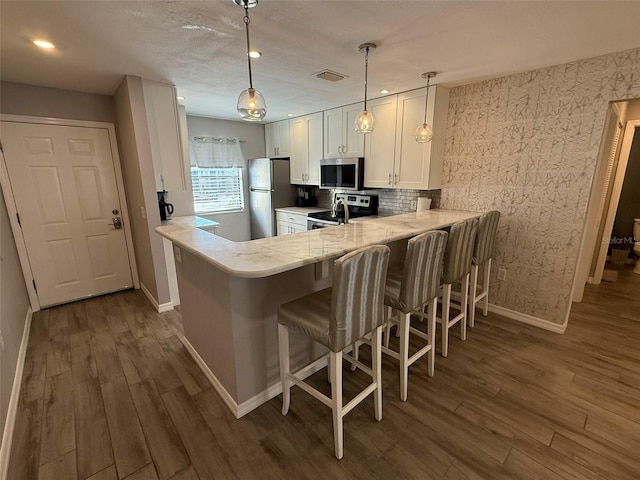 kitchen featuring white cabinetry, hanging light fixtures, dark wood-type flooring, kitchen peninsula, and appliances with stainless steel finishes