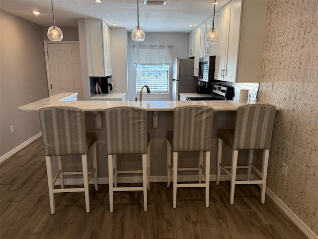 kitchen featuring kitchen peninsula, white cabinets, hanging light fixtures, and appliances with stainless steel finishes