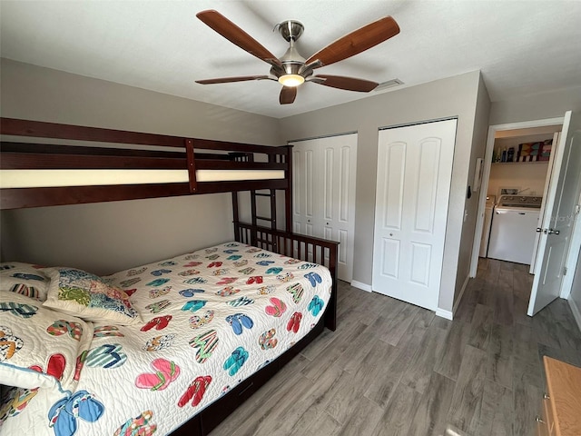 bedroom with wood-type flooring, two closets, ceiling fan, and independent washer and dryer