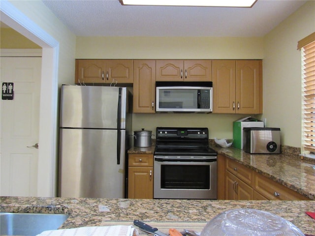 kitchen featuring light stone countertops, a textured ceiling, and appliances with stainless steel finishes