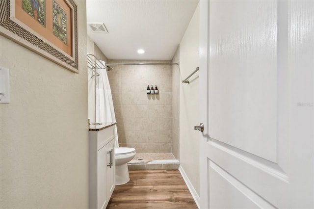 bathroom with hardwood / wood-style flooring, vanity, toilet, and tiled shower