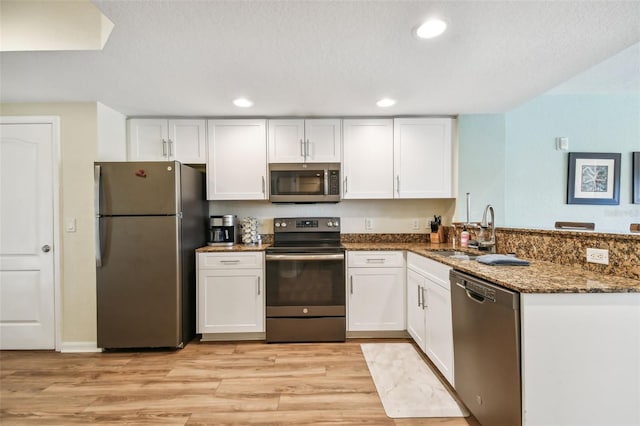 kitchen with dark stone counters, kitchen peninsula, light wood-type flooring, appliances with stainless steel finishes, and white cabinetry