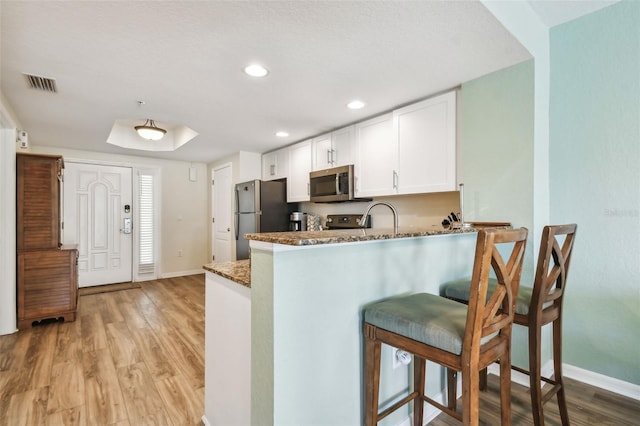 kitchen with white cabinetry, dark stone countertops, light hardwood / wood-style floors, kitchen peninsula, and stainless steel appliances