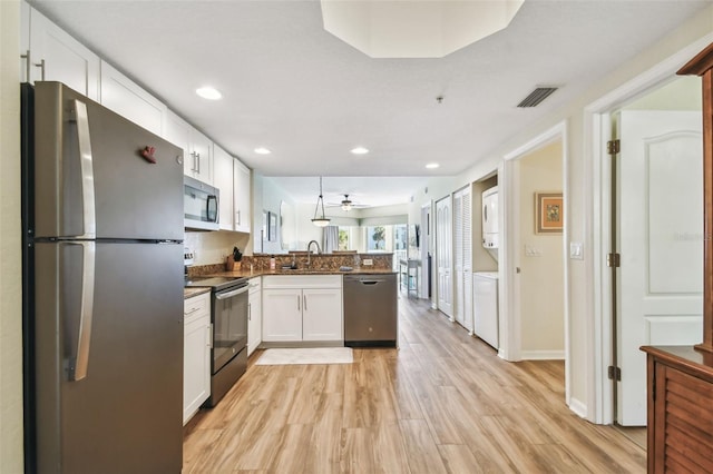 kitchen with kitchen peninsula, white cabinetry, stainless steel appliances, and stacked washer and clothes dryer