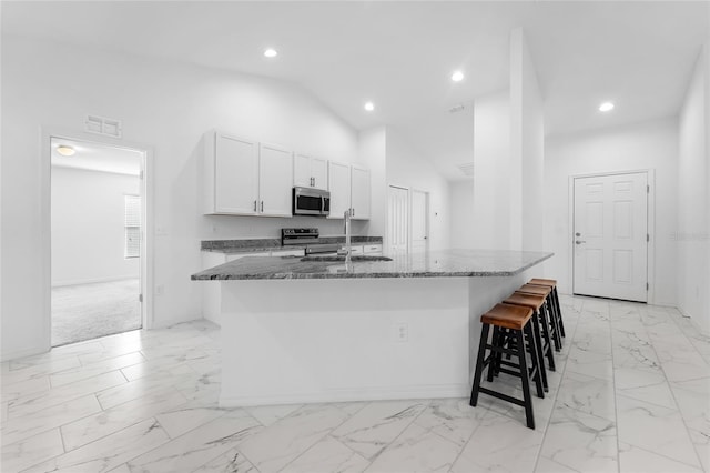 kitchen featuring stainless steel appliances, a center island with sink, stone counters, white cabinetry, and lofted ceiling