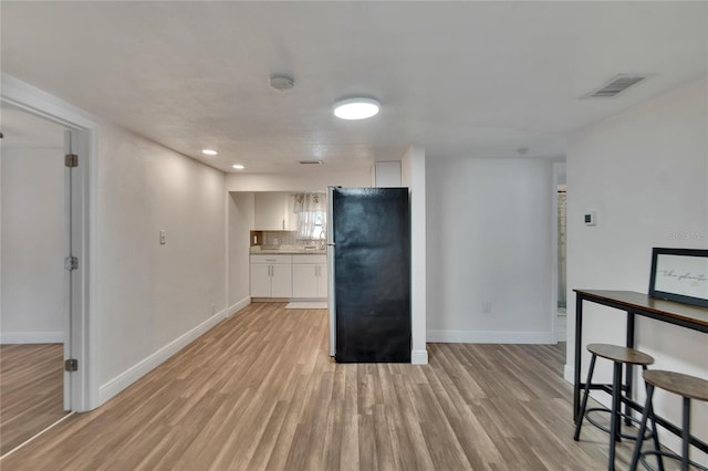 kitchen featuring white cabinets, backsplash, stainless steel refrigerator, and light hardwood / wood-style flooring