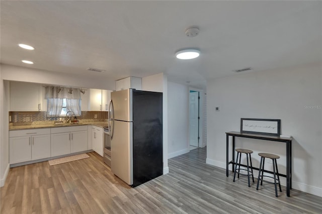 kitchen featuring a kitchen bar, appliances with stainless steel finishes, tasteful backsplash, light hardwood / wood-style floors, and white cabinetry