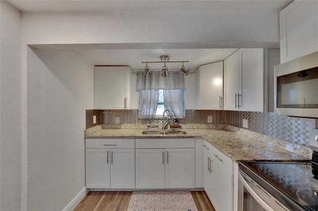 kitchen with appliances with stainless steel finishes, backsplash, sink, light hardwood / wood-style flooring, and white cabinets