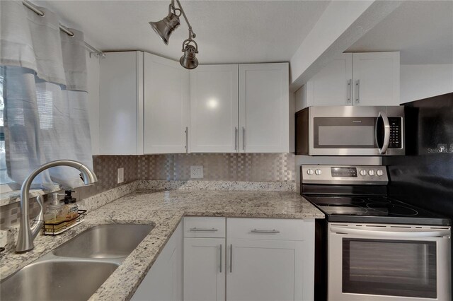 kitchen featuring sink, decorative backsplash, appliances with stainless steel finishes, light stone counters, and white cabinetry