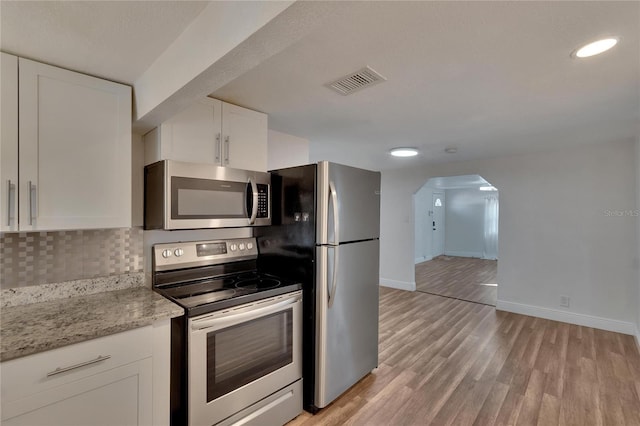 kitchen with light stone countertops, white cabinetry, stainless steel appliances, light hardwood / wood-style flooring, and decorative backsplash