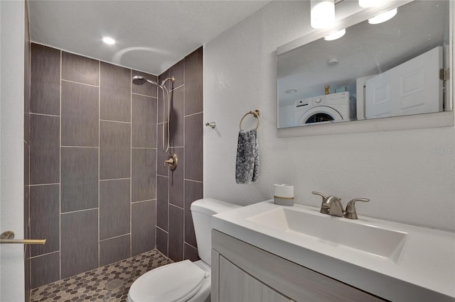 bathroom with vanity, toilet, washer / dryer, and a tile shower