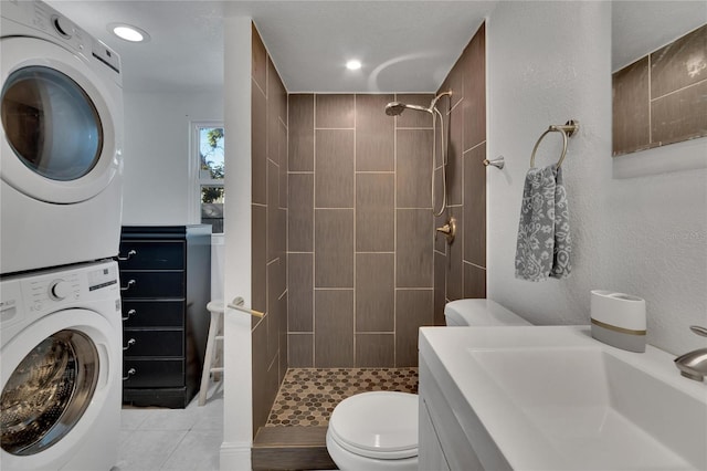 bathroom with tile patterned floors, toilet, stacked washing maching and dryer, and tiled shower