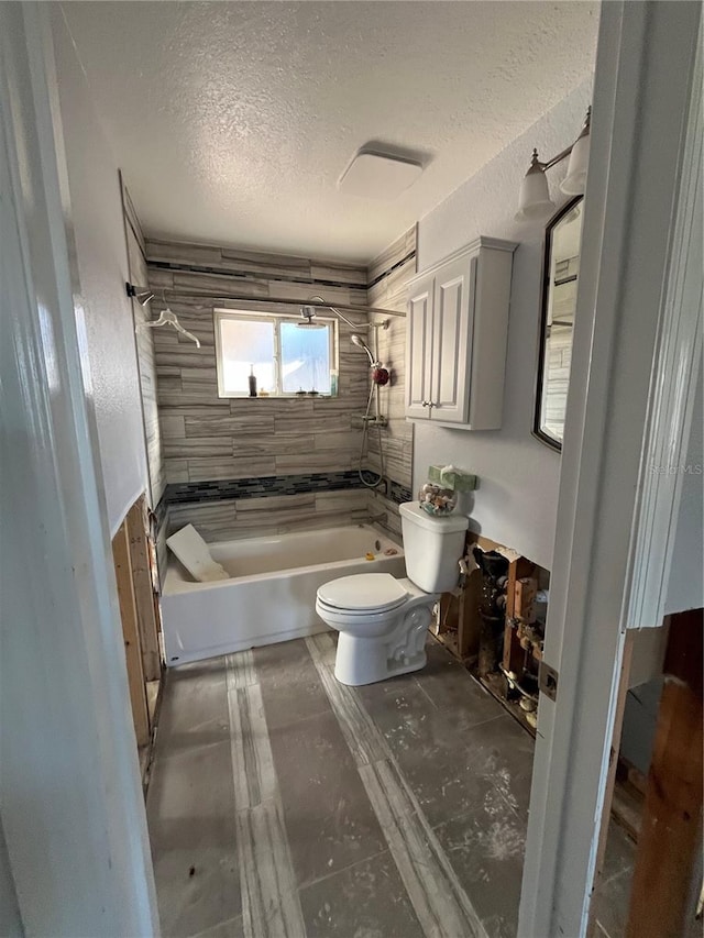 bathroom with a textured ceiling, tiled shower / bath combo, and toilet