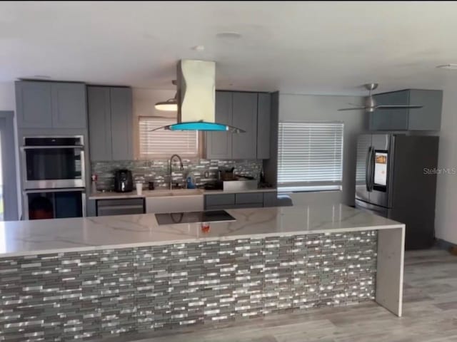 kitchen with sink, stainless steel appliances, backsplash, island exhaust hood, and light hardwood / wood-style floors