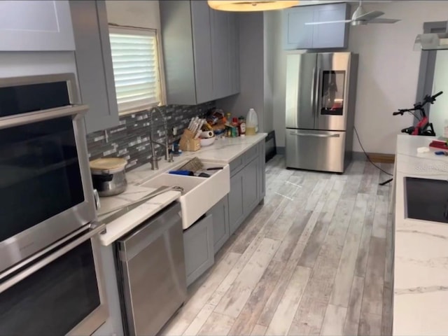 kitchen featuring decorative backsplash, appliances with stainless steel finishes, sink, gray cabinets, and light hardwood / wood-style floors