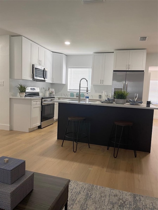 kitchen with a breakfast bar, white cabinetry, light hardwood / wood-style flooring, and appliances with stainless steel finishes