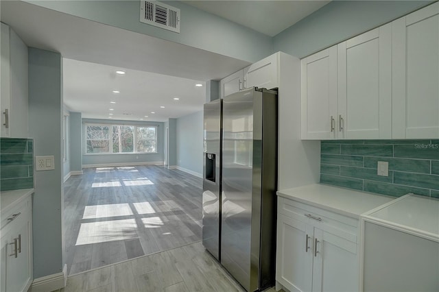 kitchen with stainless steel fridge with ice dispenser, light wood-type flooring, white cabinetry, and backsplash