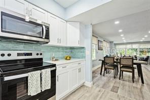 kitchen featuring tasteful backsplash, white cabinets, light hardwood / wood-style floors, and appliances with stainless steel finishes