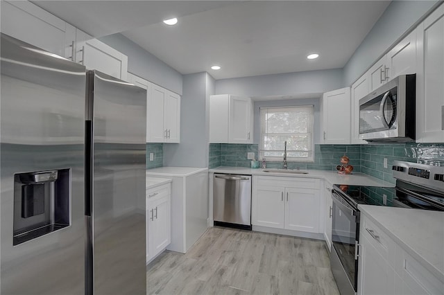 kitchen with appliances with stainless steel finishes, light wood-type flooring, tasteful backsplash, sink, and white cabinets