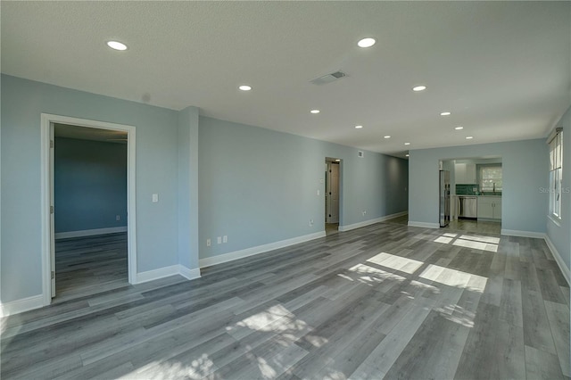 unfurnished living room with sink, a textured ceiling, and light wood-type flooring