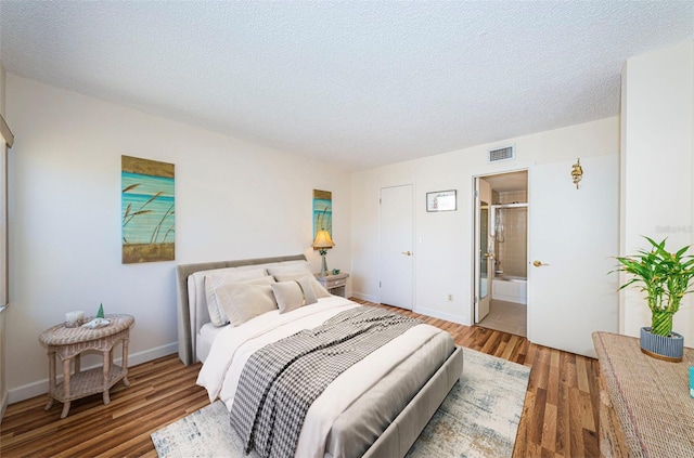 bedroom featuring ensuite bath, dark hardwood / wood-style floors, and a textured ceiling