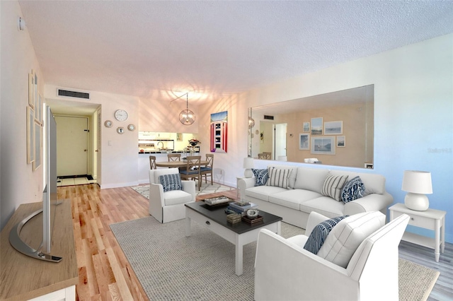 living area featuring visible vents, baseboards, light wood-style floors, and an inviting chandelier