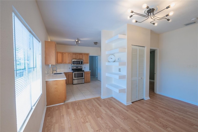 kitchen featuring decorative backsplash, a chandelier, light wood-type flooring, and appliances with stainless steel finishes