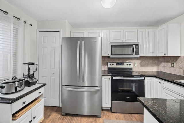 kitchen featuring white cabinets, light hardwood / wood-style flooring, dark stone countertops, appliances with stainless steel finishes, and tasteful backsplash