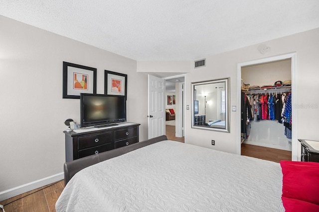 bedroom featuring wood-type flooring, a textured ceiling, a spacious closet, and a closet