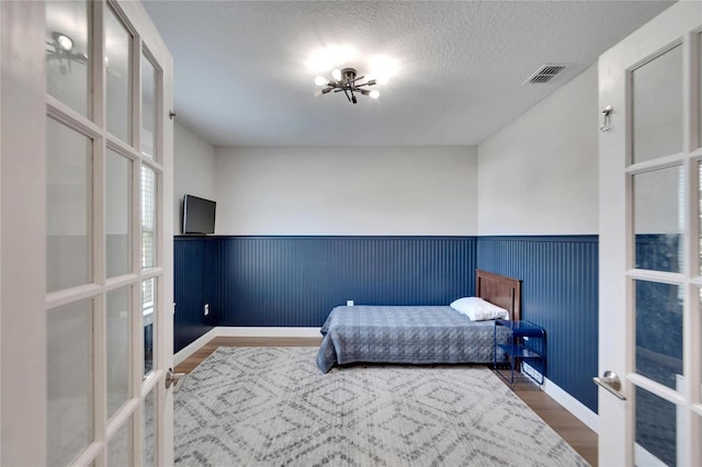 bedroom featuring a chandelier, french doors, wood-type flooring, and a textured ceiling