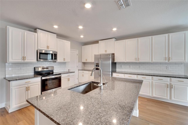 kitchen with light wood-type flooring, stainless steel appliances, a kitchen island with sink, sink, and white cabinets