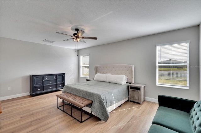 bedroom featuring a textured ceiling, light hardwood / wood-style floors, multiple windows, and ceiling fan