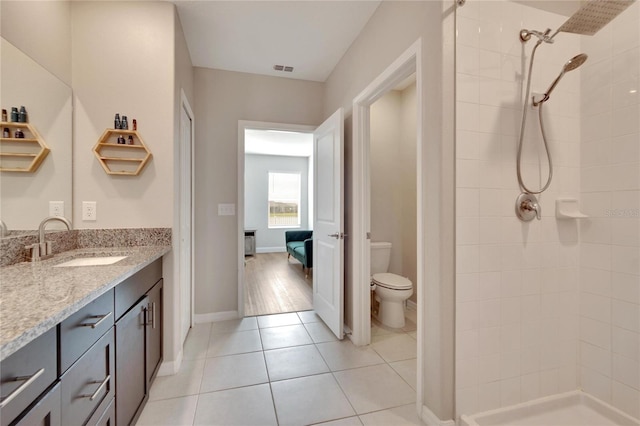 bathroom with tiled shower, tile patterned flooring, vanity, and toilet