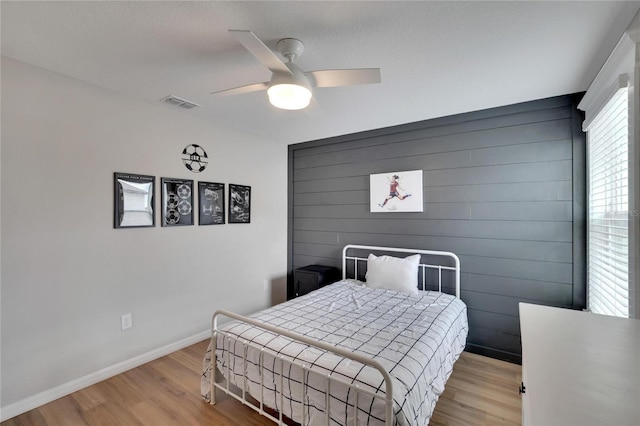 bedroom with ceiling fan, light hardwood / wood-style floors, and wood walls