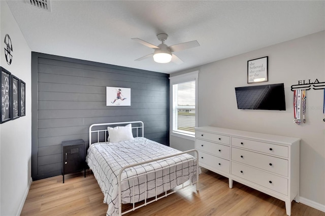 bedroom with light wood-type flooring, ceiling fan, and wood walls