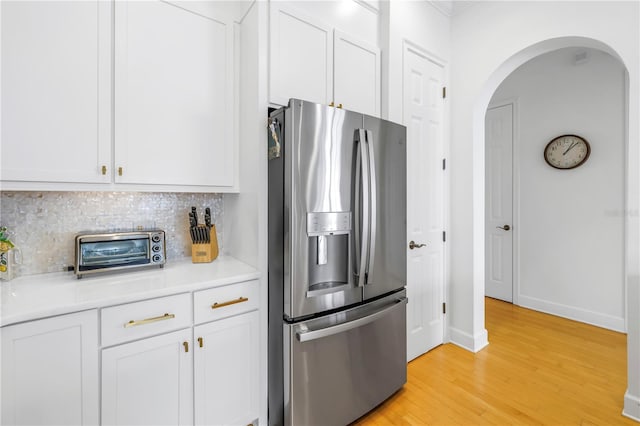 kitchen with tasteful backsplash, white cabinets, stainless steel refrigerator with ice dispenser, and light wood-type flooring