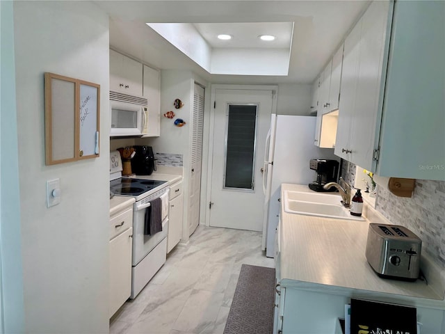 kitchen with a raised ceiling, sink, white cabinets, and white appliances