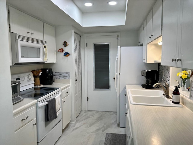 kitchen with white appliances, backsplash, a raised ceiling, sink, and white cabinetry