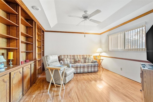 living room with a tray ceiling, ceiling fan, crown molding, and light hardwood / wood-style floors