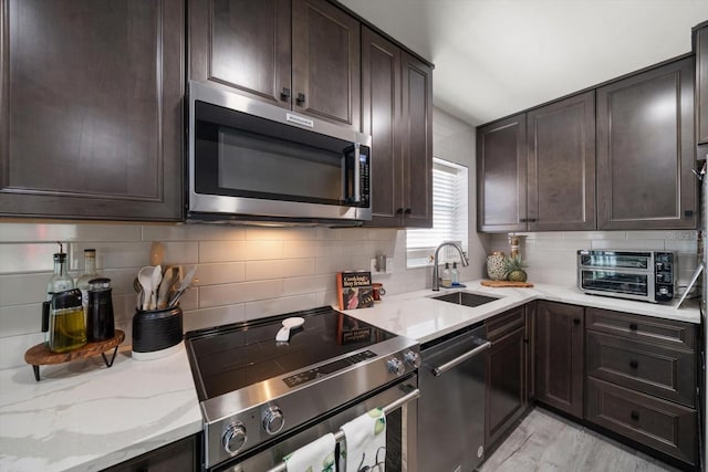 kitchen with light stone countertops, appliances with stainless steel finishes, dark brown cabinets, sink, and light hardwood / wood-style floors