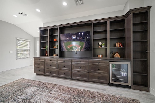 bar with light hardwood / wood-style floors, dark brown cabinetry, beverage cooler, and vaulted ceiling