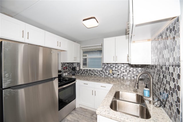 kitchen with light stone countertops, backsplash, stainless steel appliances, sink, and white cabinetry