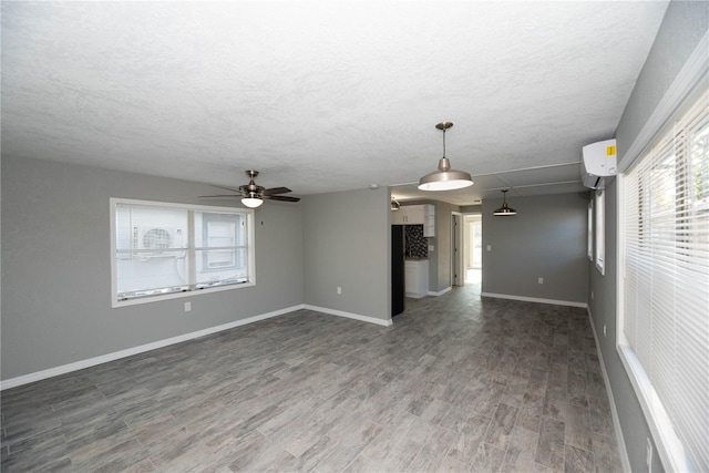 empty room featuring a textured ceiling, ceiling fan, a healthy amount of sunlight, and dark hardwood / wood-style floors