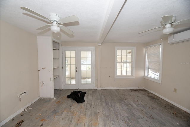 spare room featuring french doors, a textured ceiling, a wall unit AC, ceiling fan, and wood-type flooring